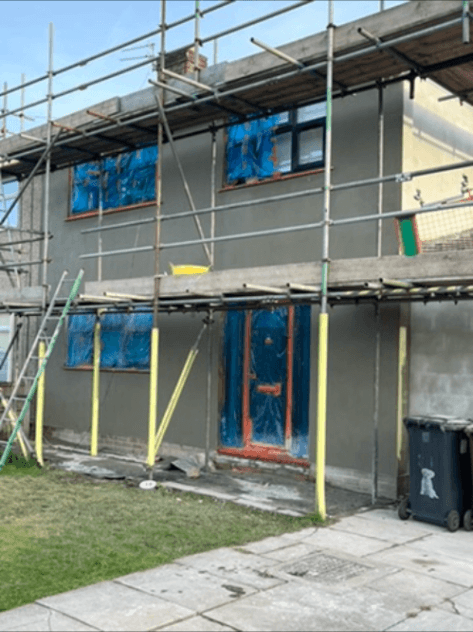 Scaffolded two-storey house mid-render, windows taped for protection